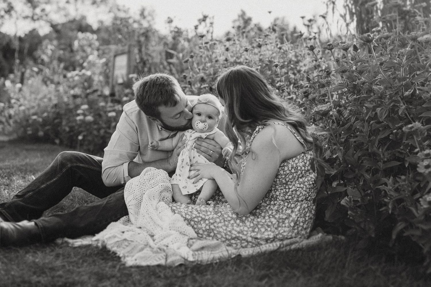 Black and white family portrait on blanket surrounded by flowering garden.