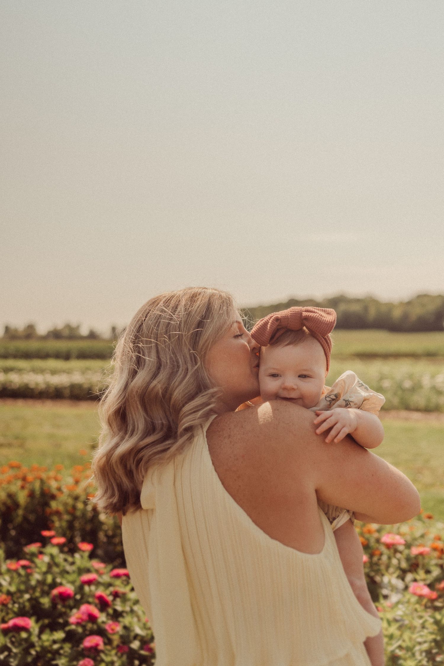 Mother and baby share a tender moment in a flower garden at sunset.