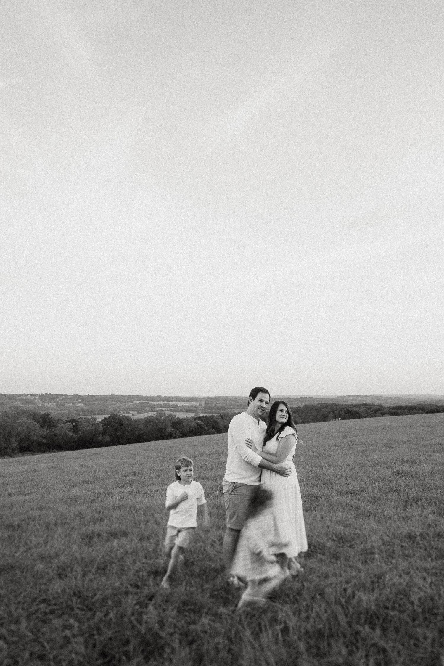 Black and white portrait of a family enjoying a playful moment on a rolling hill.