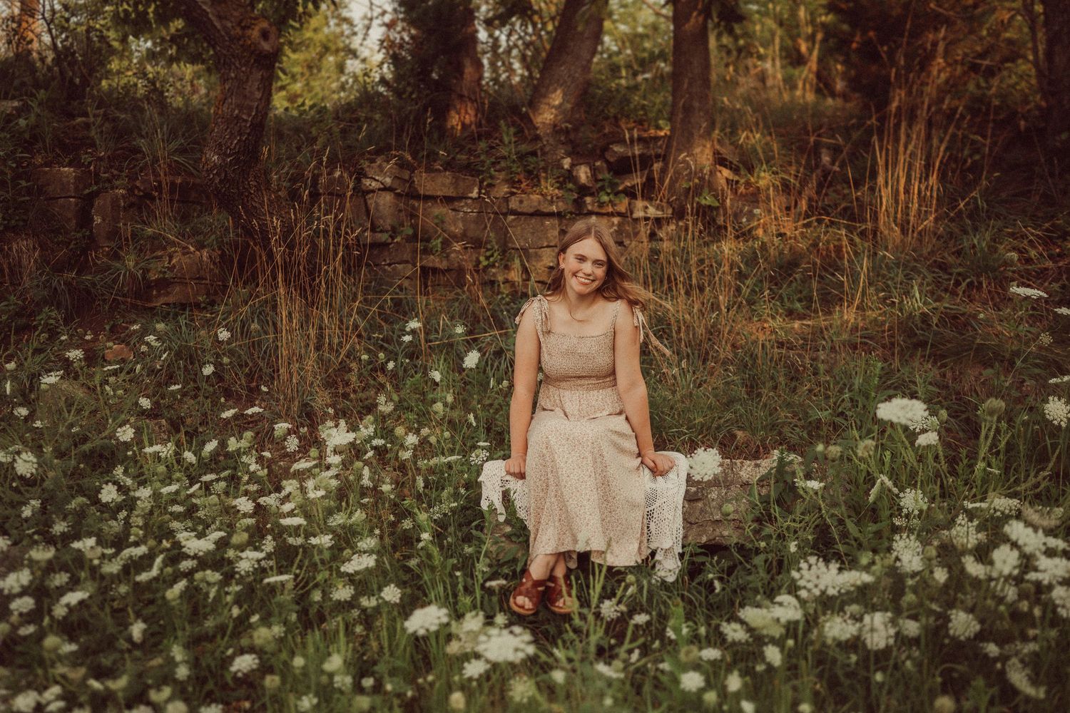 A vintage-inspired outdoor portrait surrounded by white wildflowers and stone wall in warm tones.
