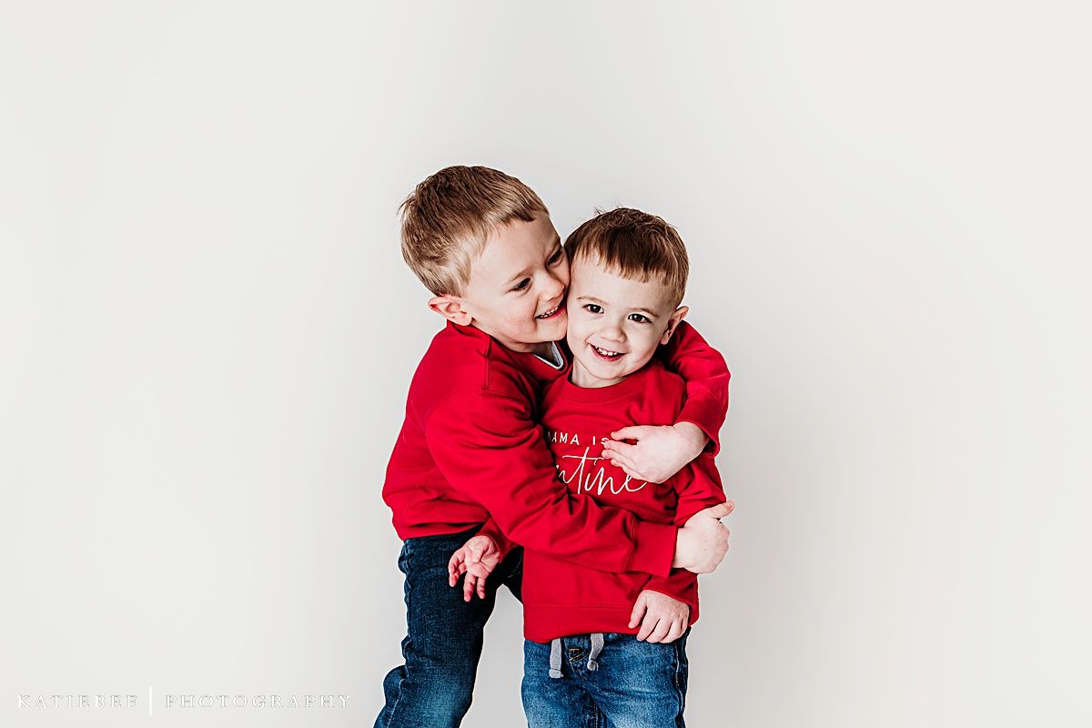 Playful moment captured between two in matching red sweaters against white backdrop.