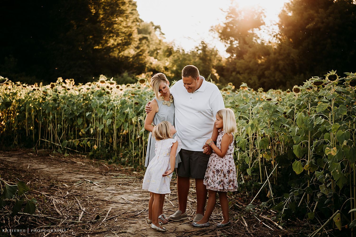 Family enjoying a warm summer evening together among tall sunflowers on a dirt path.