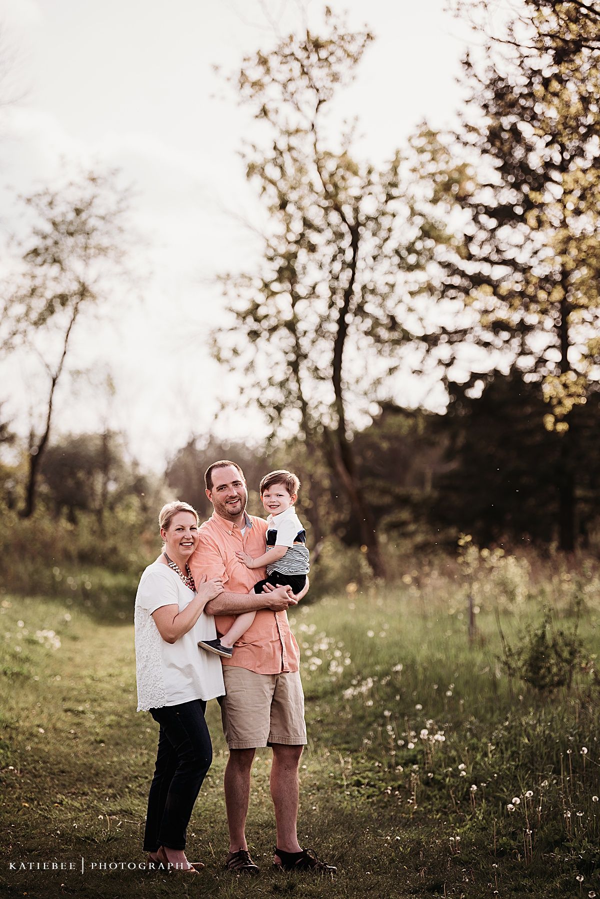 A joyful outdoor portrait of three people standing together under blooming trees in a field.