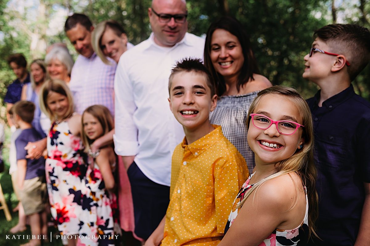 Group portrait of family members smiling outdoors with greenery in background.