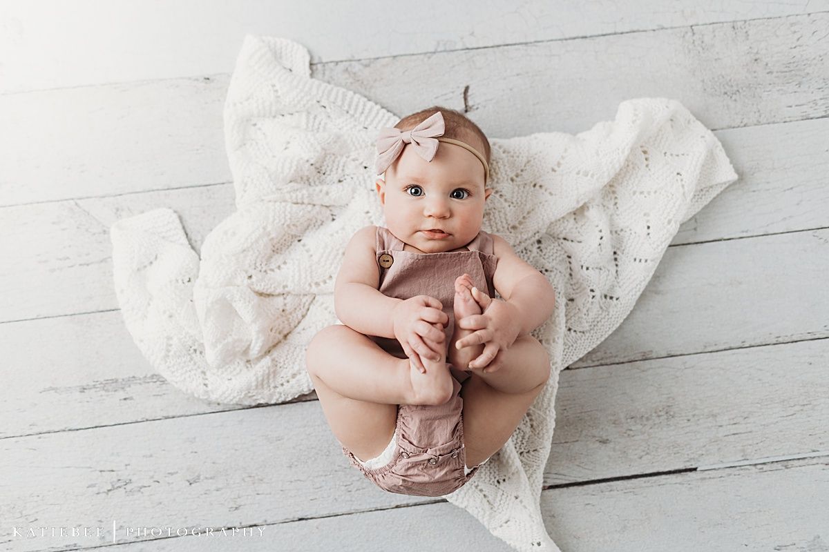 Baby in pink outfit lying on white textured blanket during portrait session.