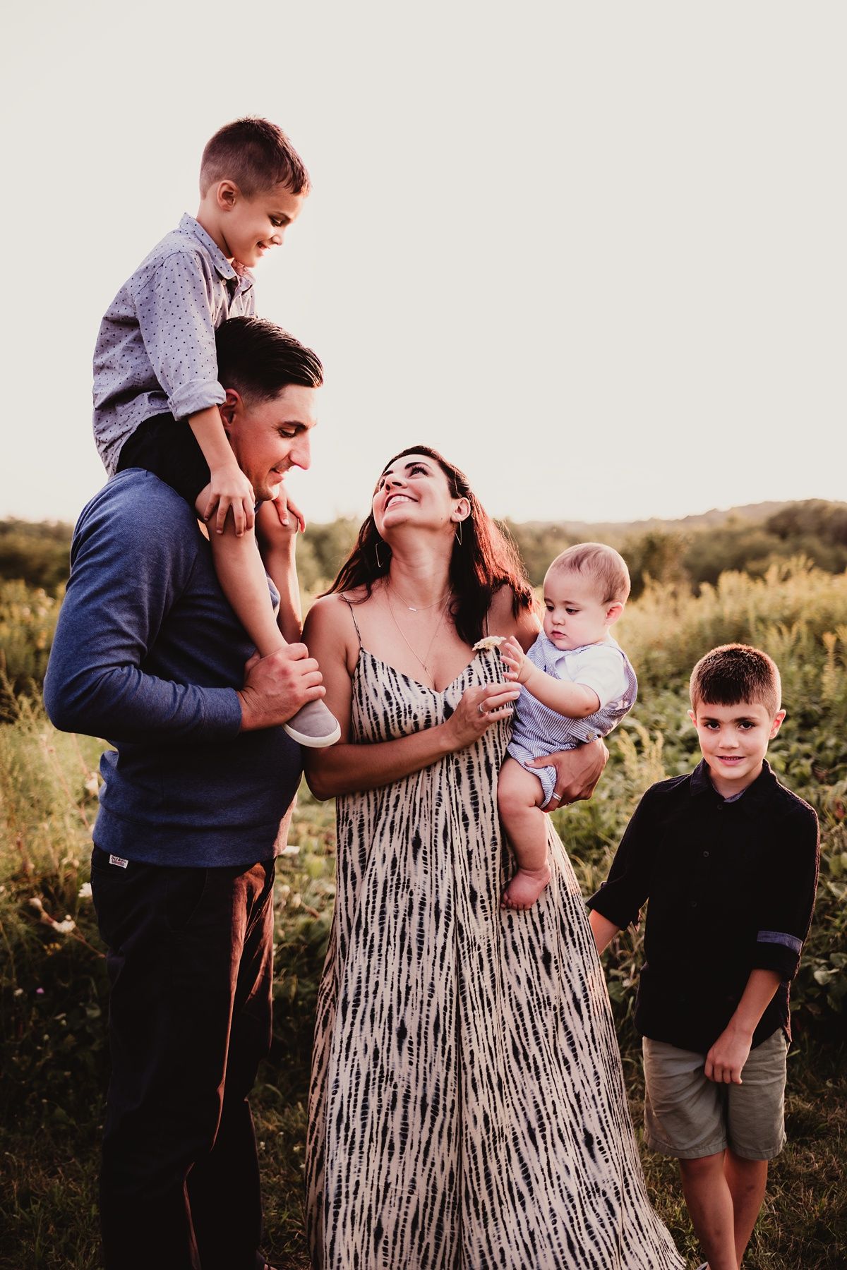 A candid outdoor family portrait in a field at sunset with everyone laughing and embracing.