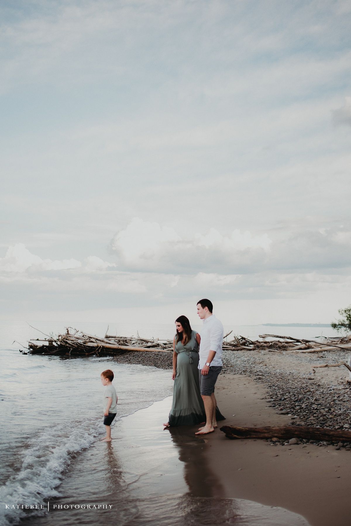 A family stands together on a beach with driftwood and cloudy skies in the background.