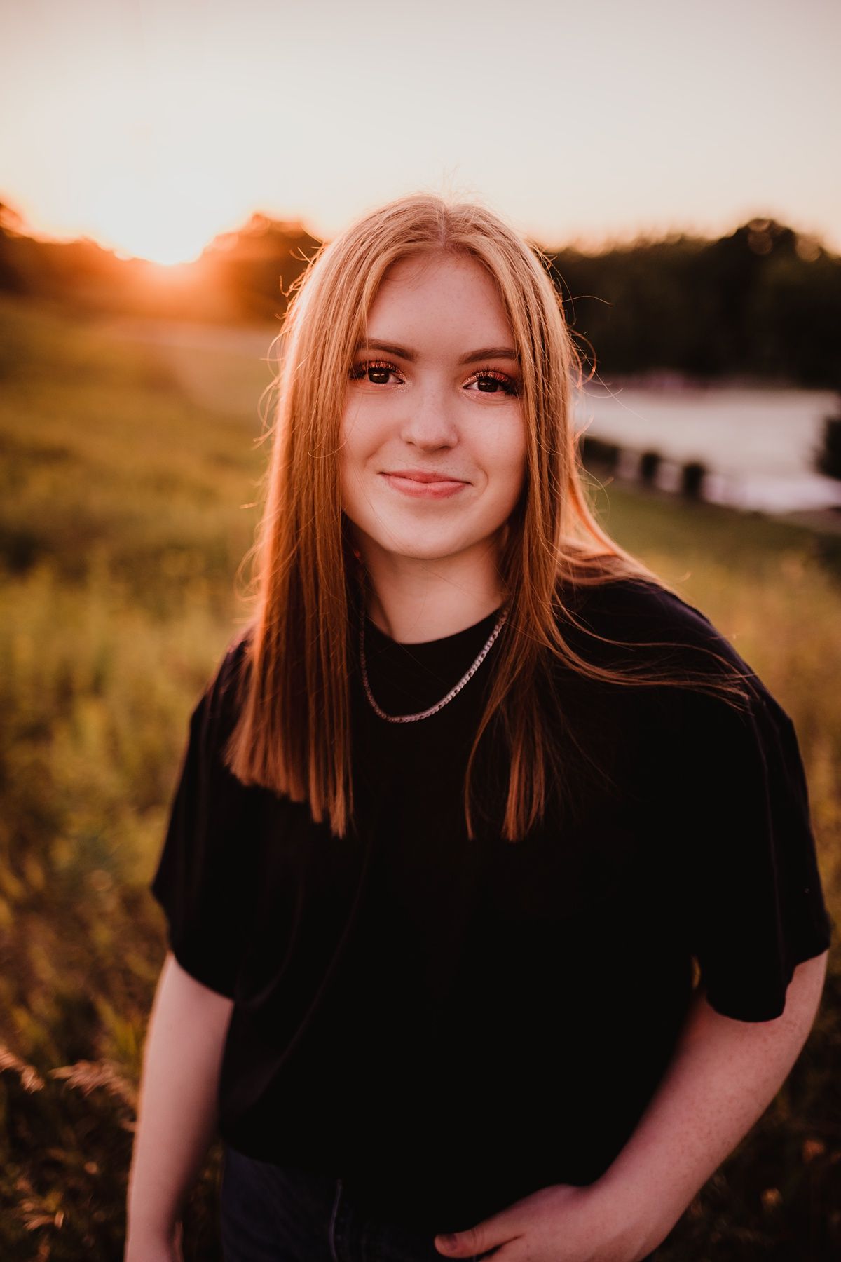 Portrait of someone in a black shirt against a golden sunset with natural field backdrop.