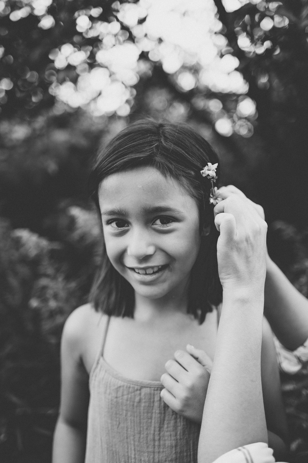 Black and white portrait of someone in a gray dress holding a small flower with bokeh background.