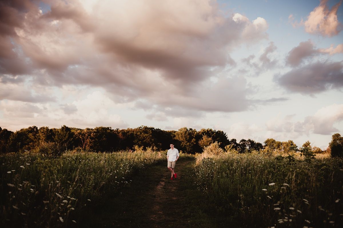 A person walking through a tall grass meadow at sunset with dramatic clouds overhead.