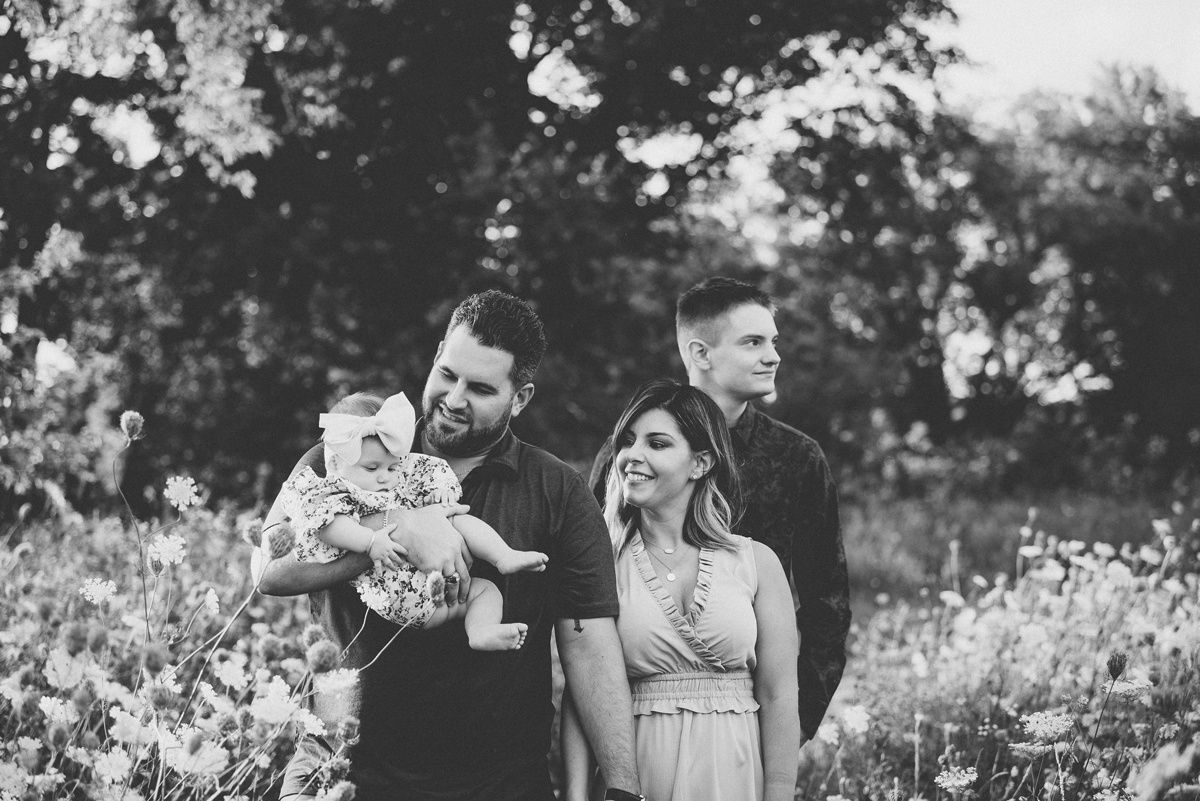 A black and white portrait of a family standing together in a meadow of wildflowers.