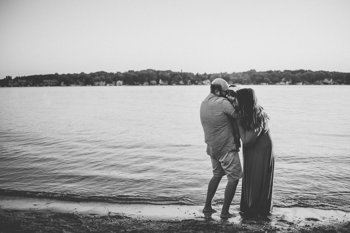 Black and white silhouette of couple embracing while standing at the edge of a tranquil lake.