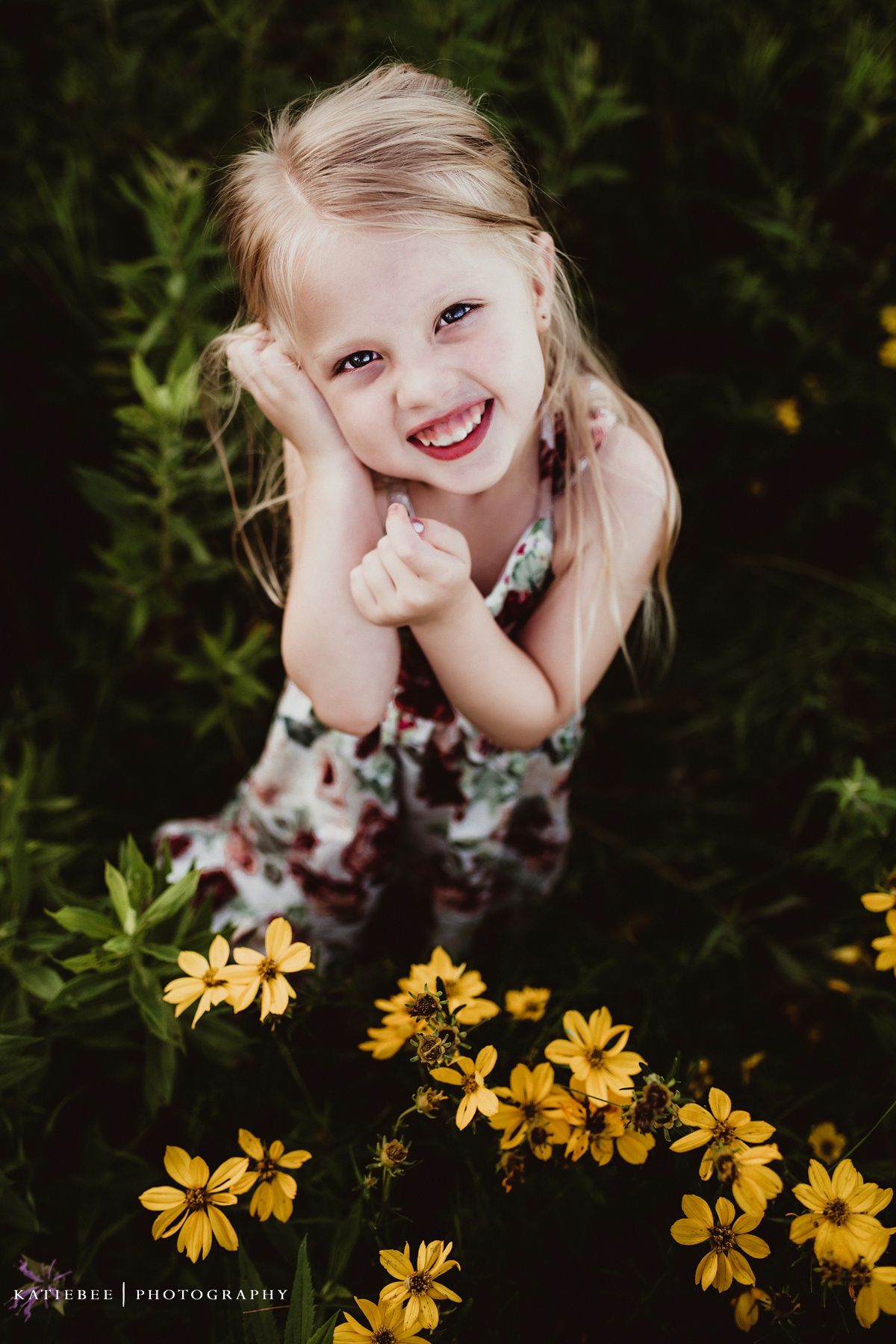Young child poses cheerfully among yellow wildflowers in an outdoor portrait session.