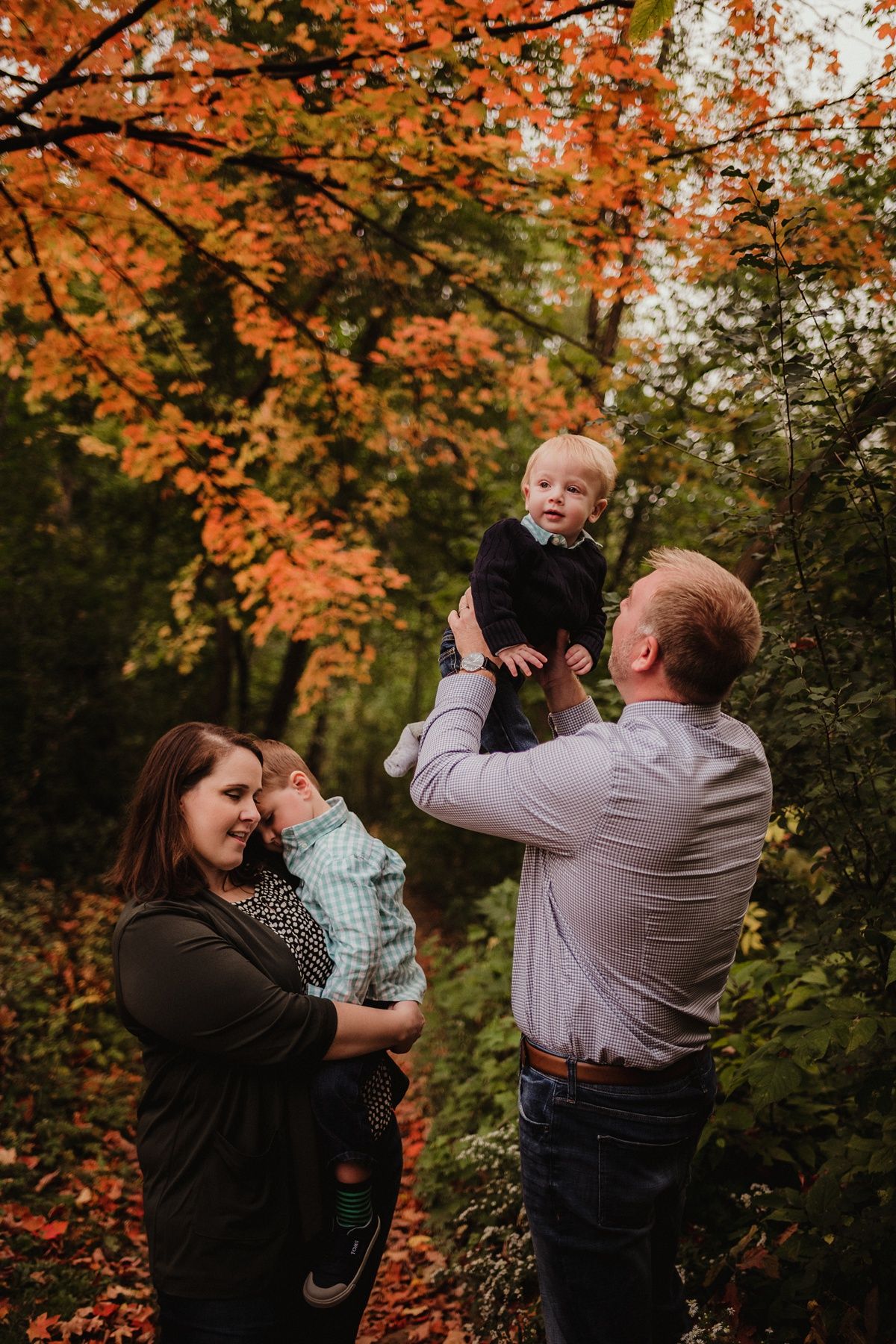Family playing and lifting children together in vibrant autumn forest setting.