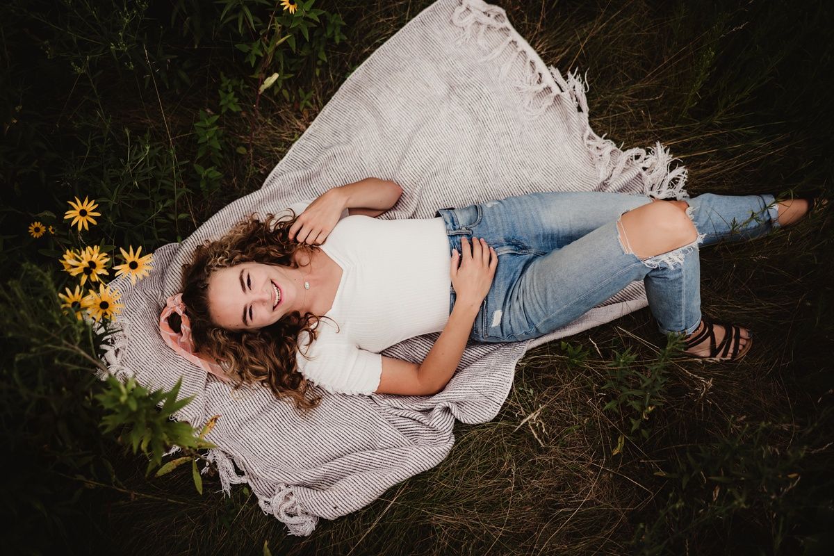 Overhead shot of person lying on white blanket surrounded by yellow flowers.