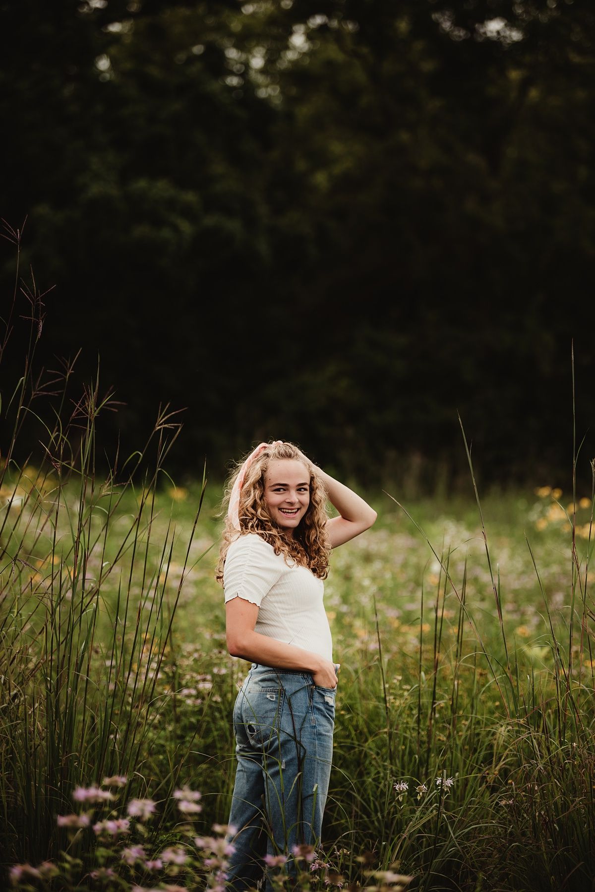 Artistic outdoor portrait among tall grasses and wildflowers at golden hour.