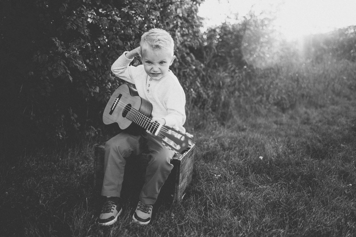 Black and white photo of child playing guitar while sitting outdoors.