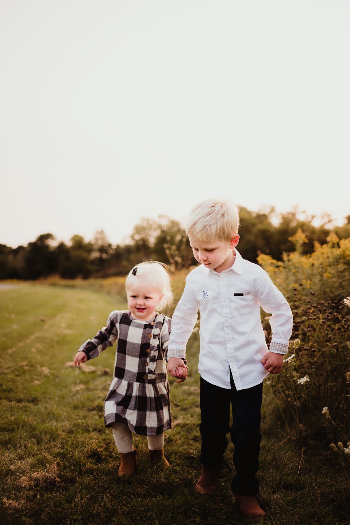 Two children holding hands and running through a golden field at sunset in autumn.