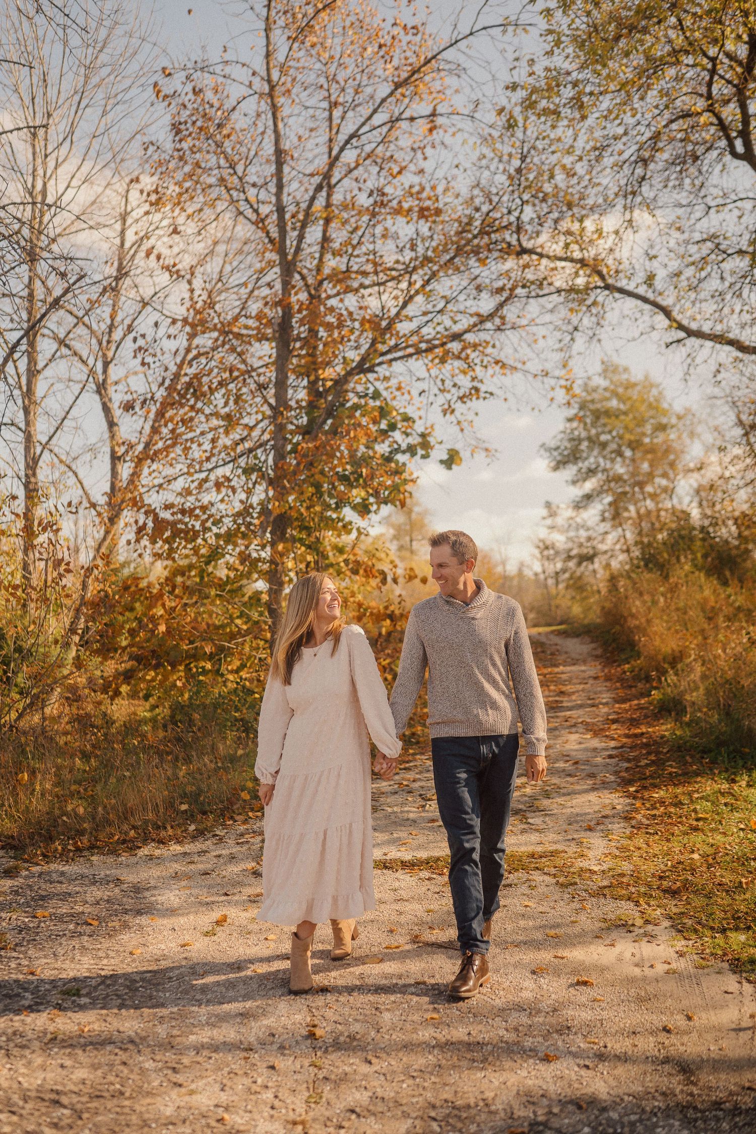 A couple walking hand in hand on a dirt path surrounded by golden autumn trees.