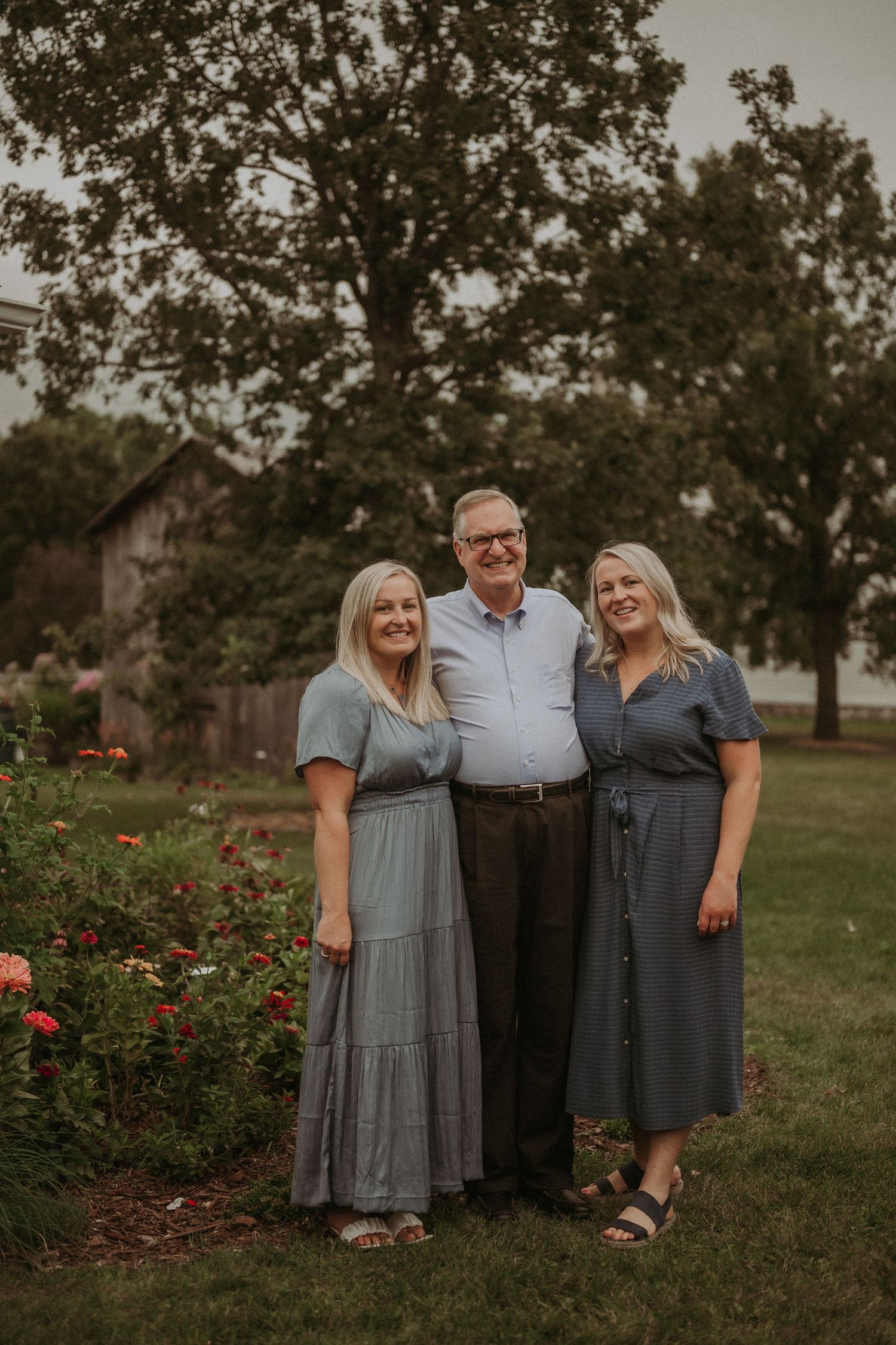 Three people pose together in front of a rose garden during golden hour.