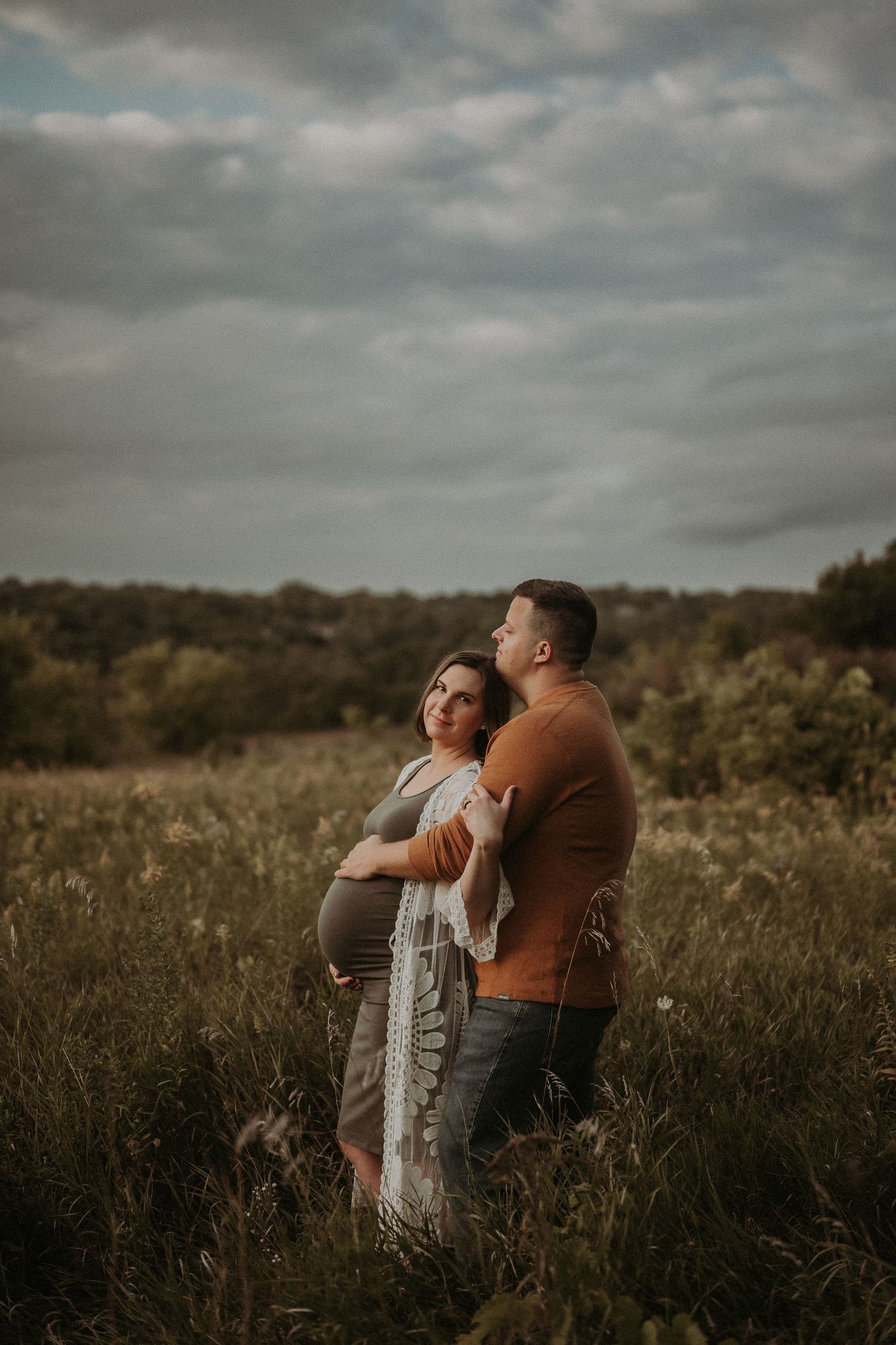 Romantic maternity photo of a couple embracing in a golden field during sunset.