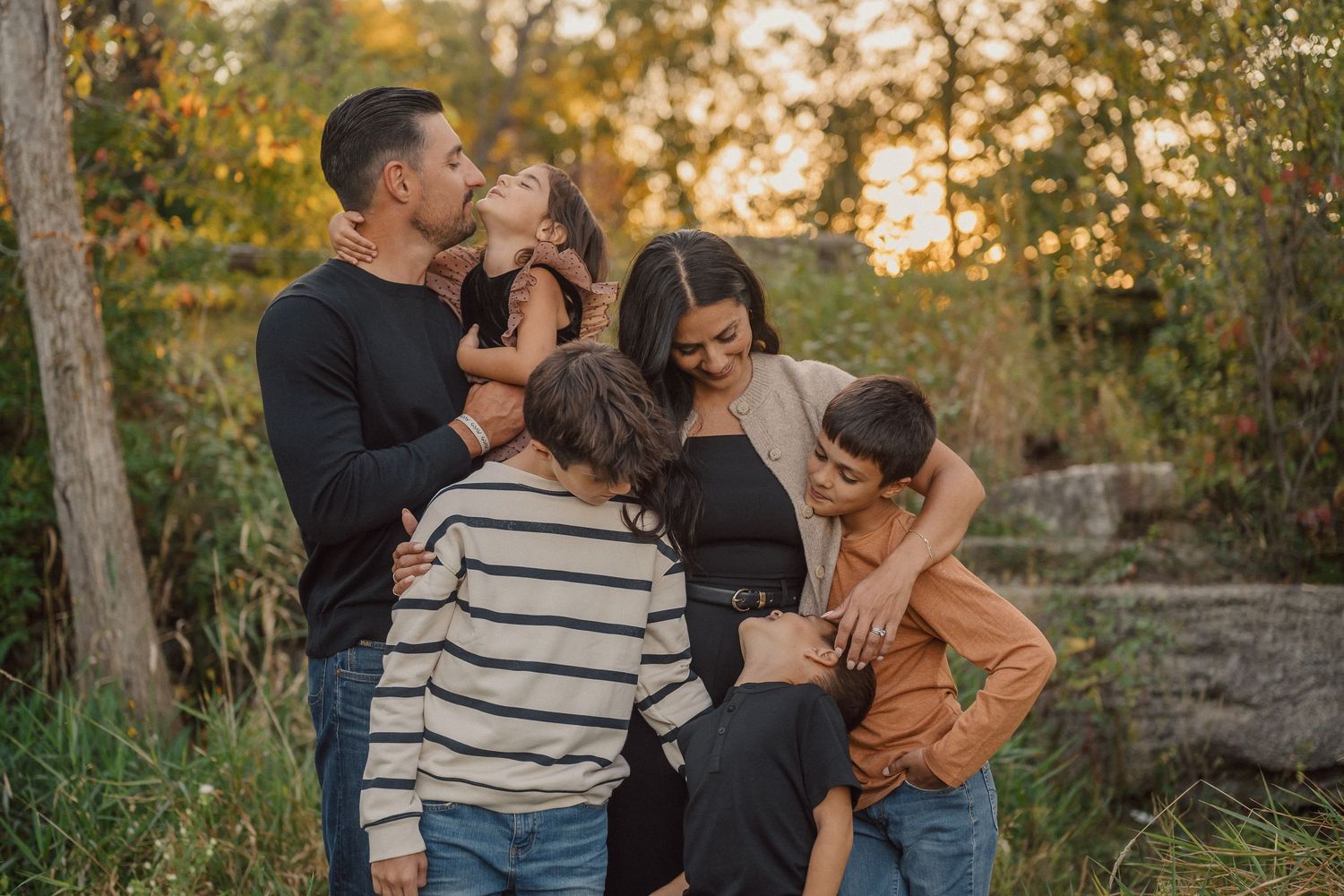 A family shares joyful moments together during a golden hour photoshoot in a wooded outdoor setting.