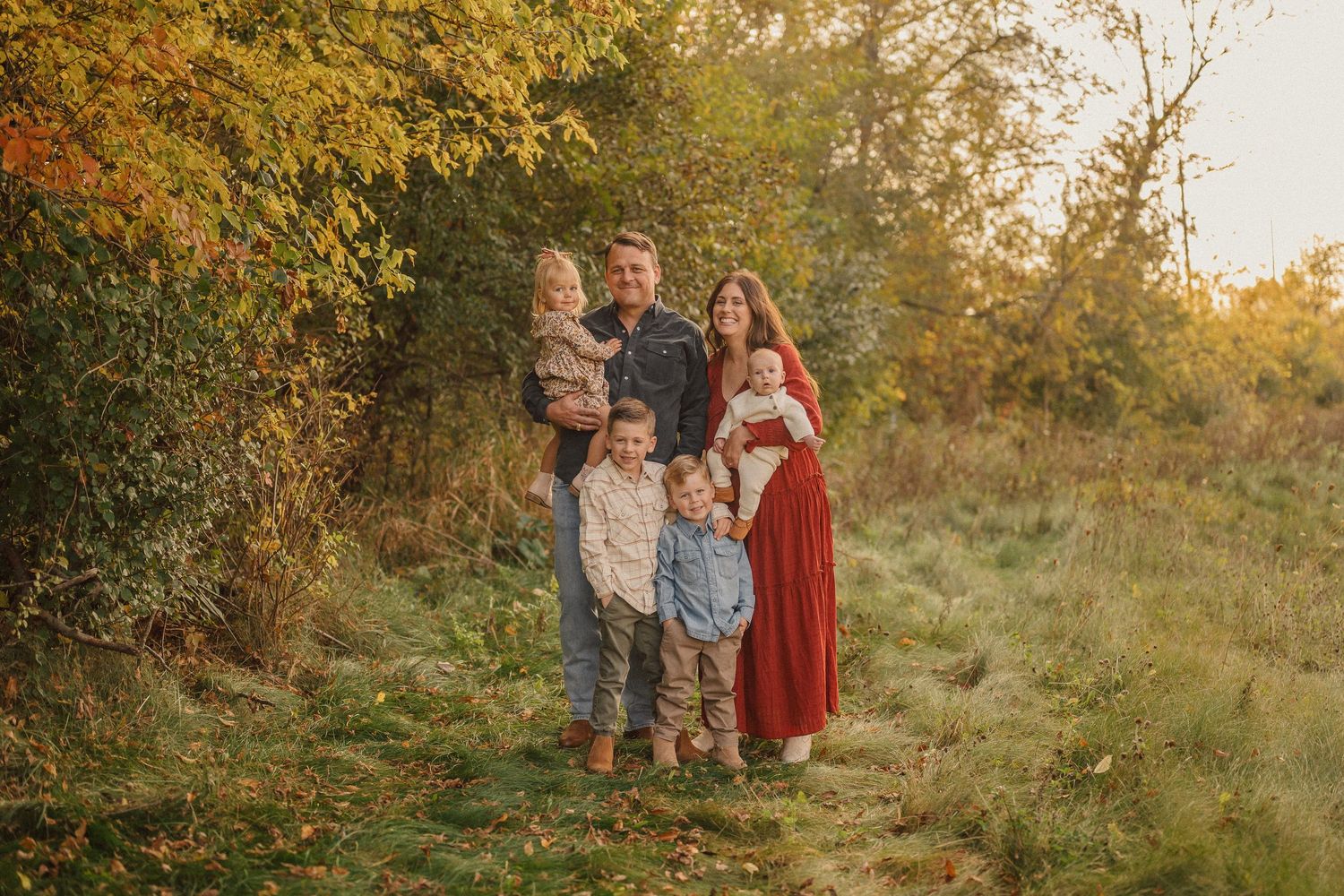 Family poses together in autumn field during golden hour sunset photography session.