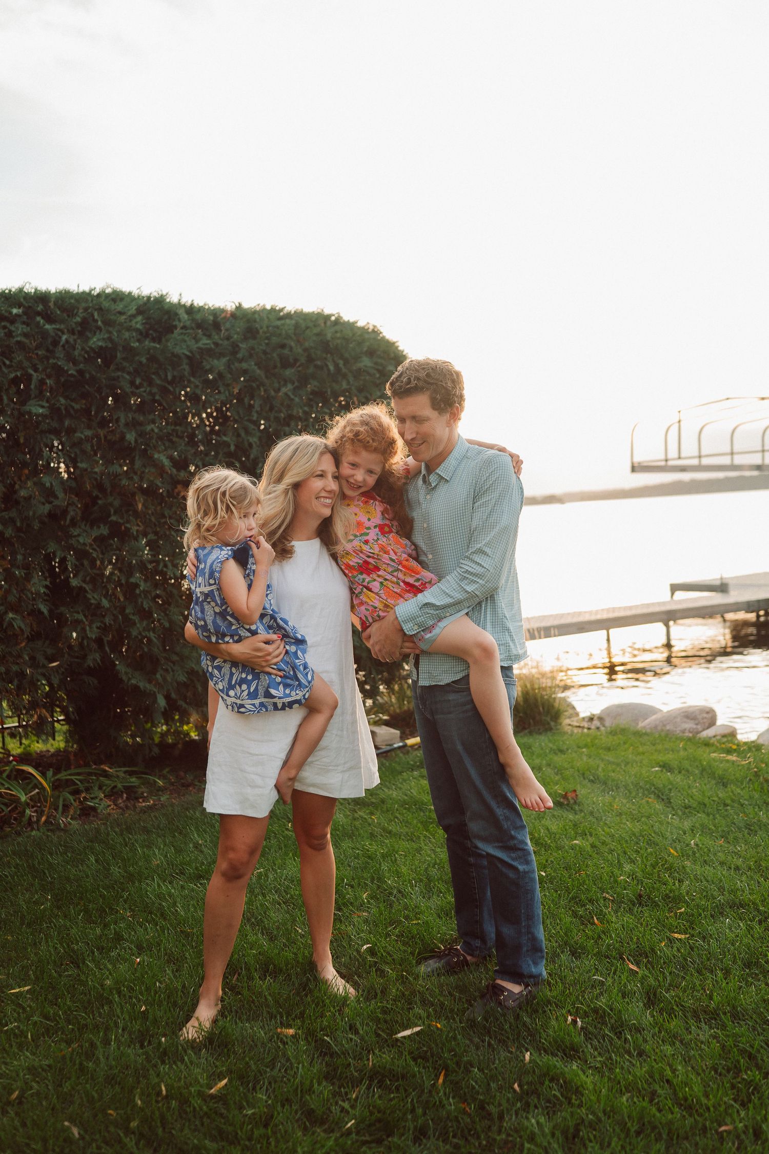A family shares a tender moment together on a grassy lawn near water during golden hour.