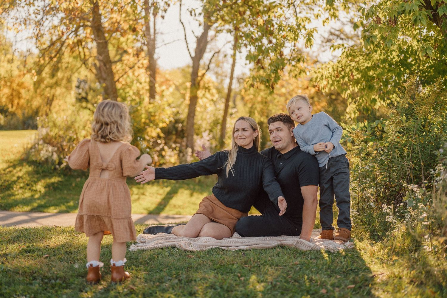 Family group enjoys outdoor photo session in park setting with golden sunlight filtering through trees.