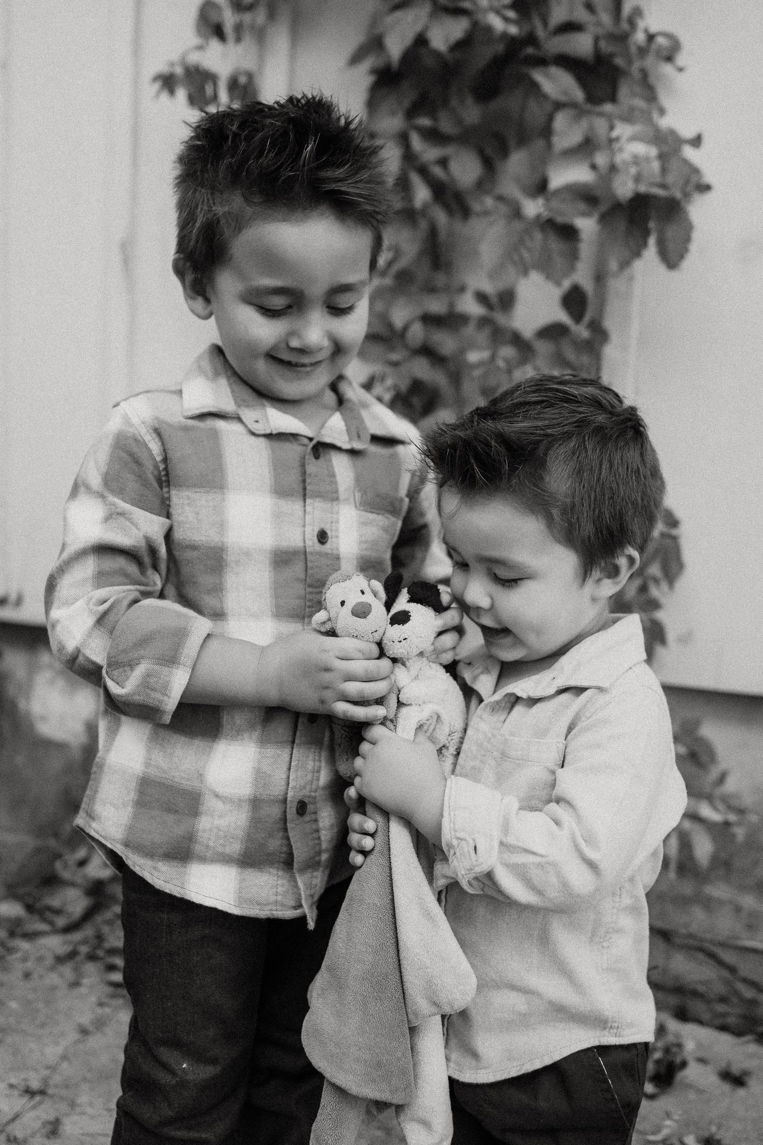 Two young children in plaid shirts share a tender moment while playing outdoors in this vintage black and white photograph.