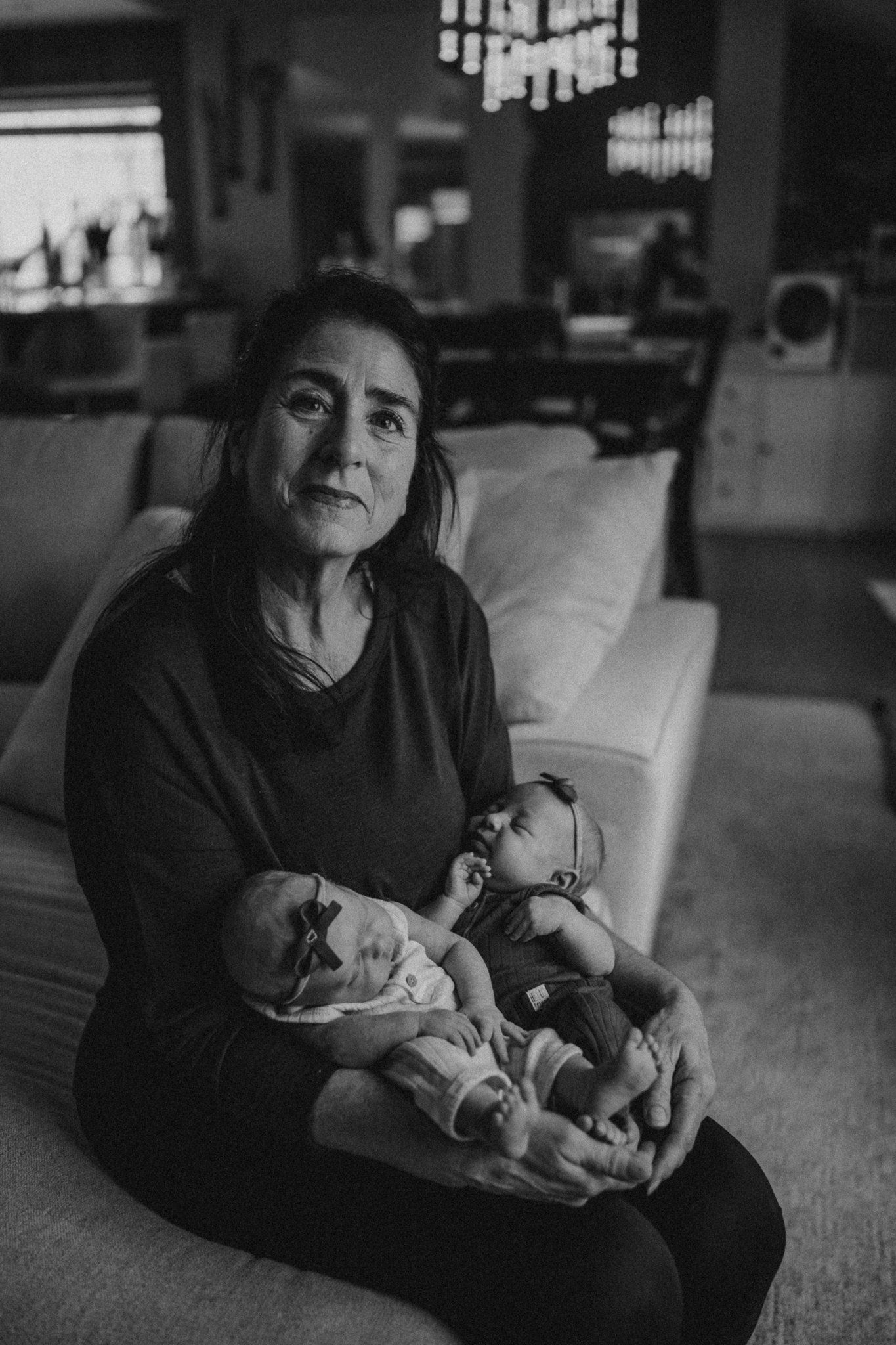 A monochrome portrait of a caregiver holding twin infants on a comfortable couch.