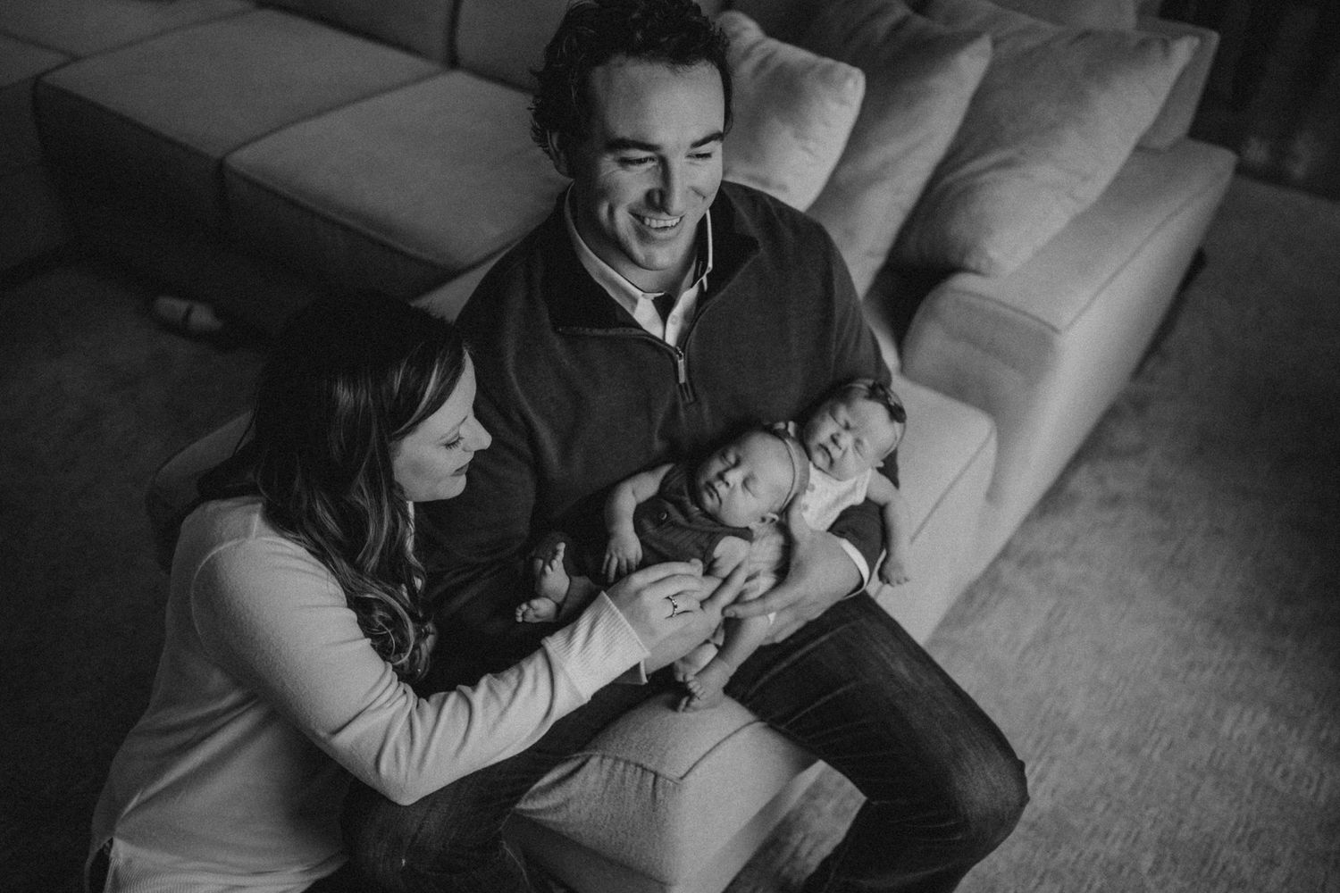 Parents sitting on couch holding newborn baby in black and white photography.