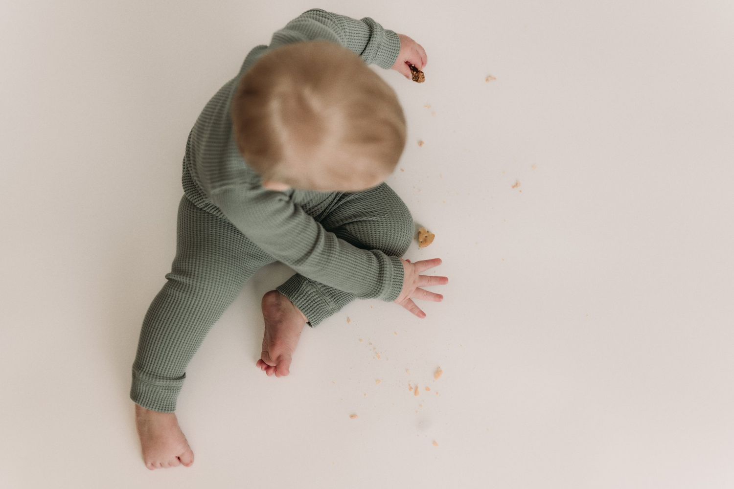 Close up of baby's legs in green ribbed pants on light backdrop.