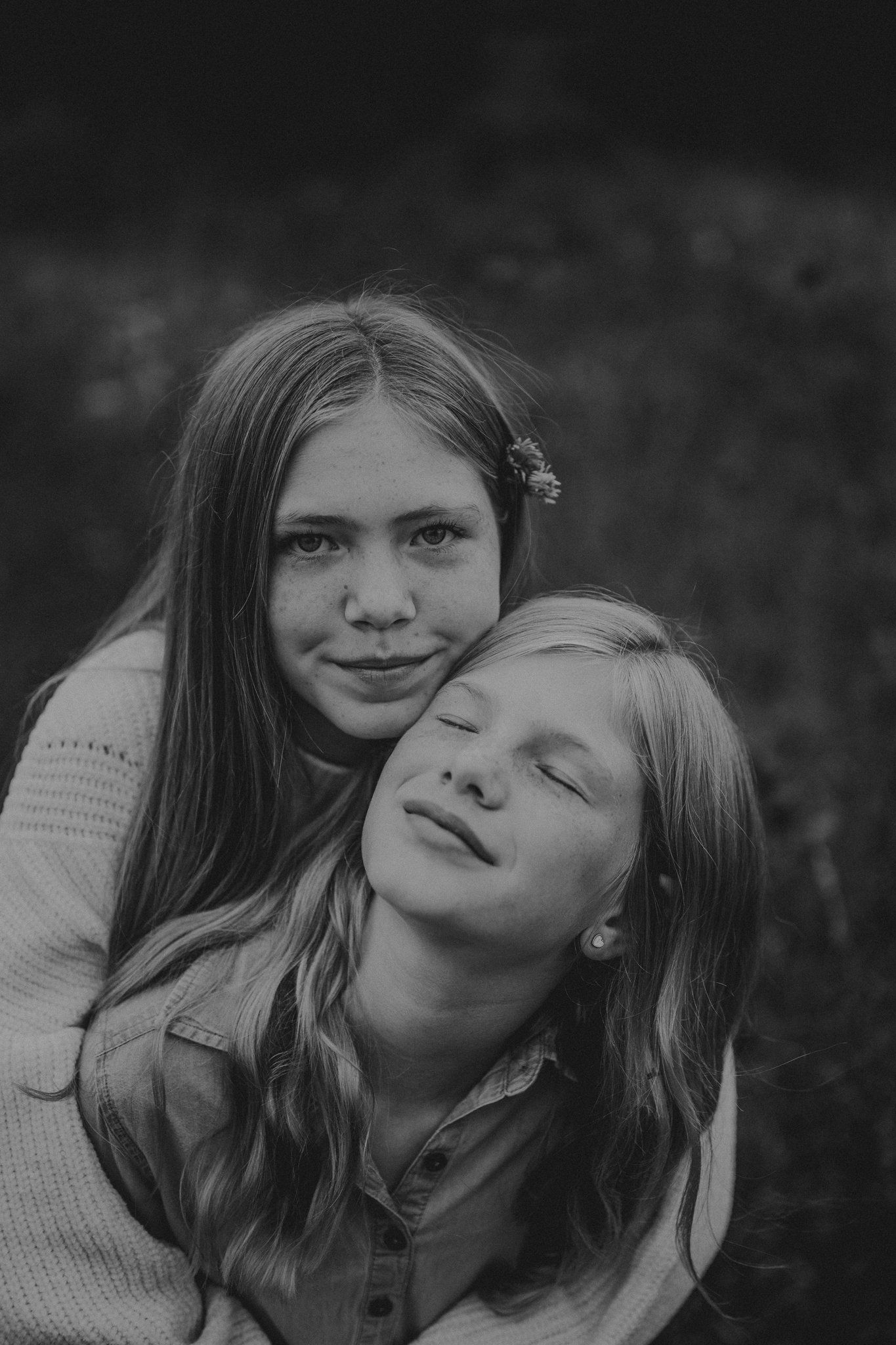 A black and white portrait of two people sharing a tender embrace outdoors.