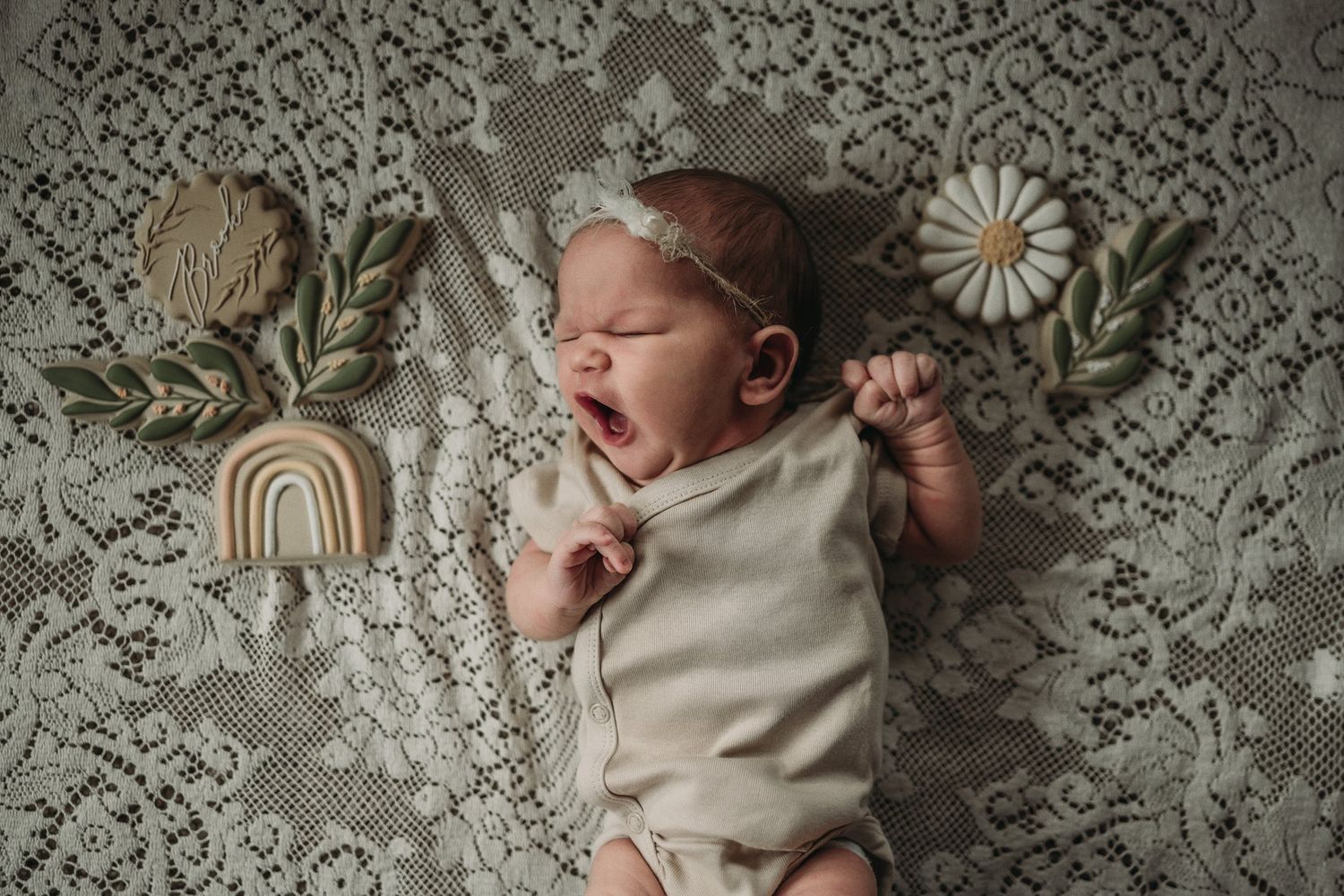 Newborn lying on intricate lace fabric with boho rainbow and daisy decorative elements.