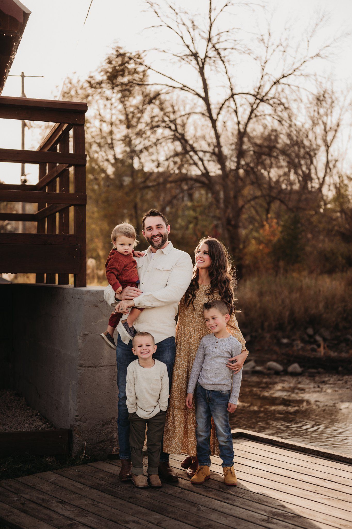A family poses together on a wooden deck during autumn sunset.