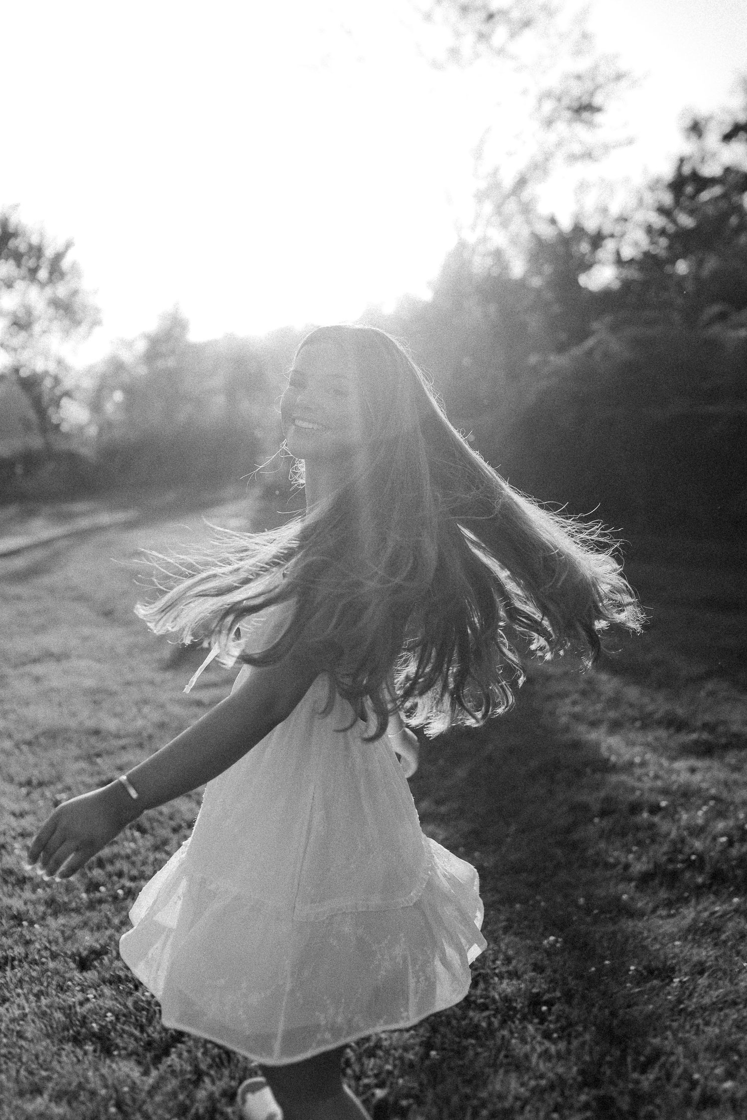 A black and white action shot of spinning and twirling in a white dress at sunset.