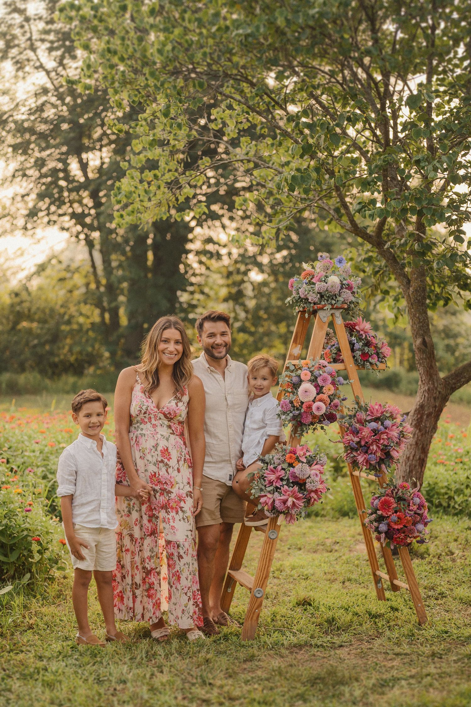 A summer family portrait in a lush green field with a decorative wooden ladder displaying colorful floral arrangements.