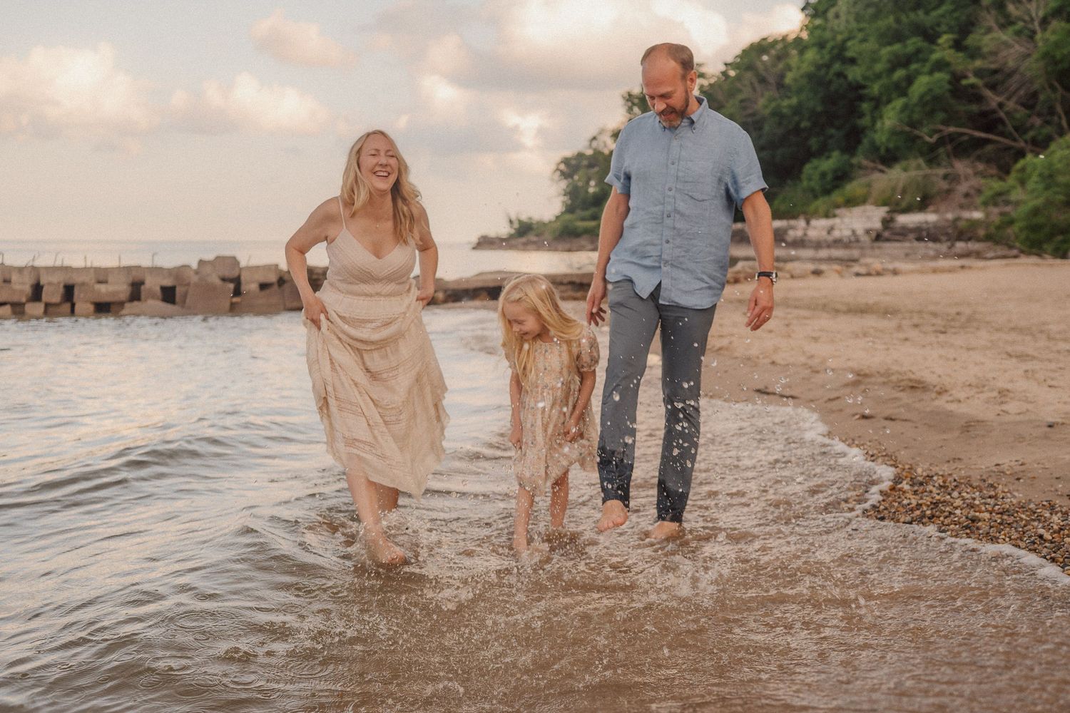 A family splashing and playing in shallow ocean waves at sunset along a beach with cliffs in the background.