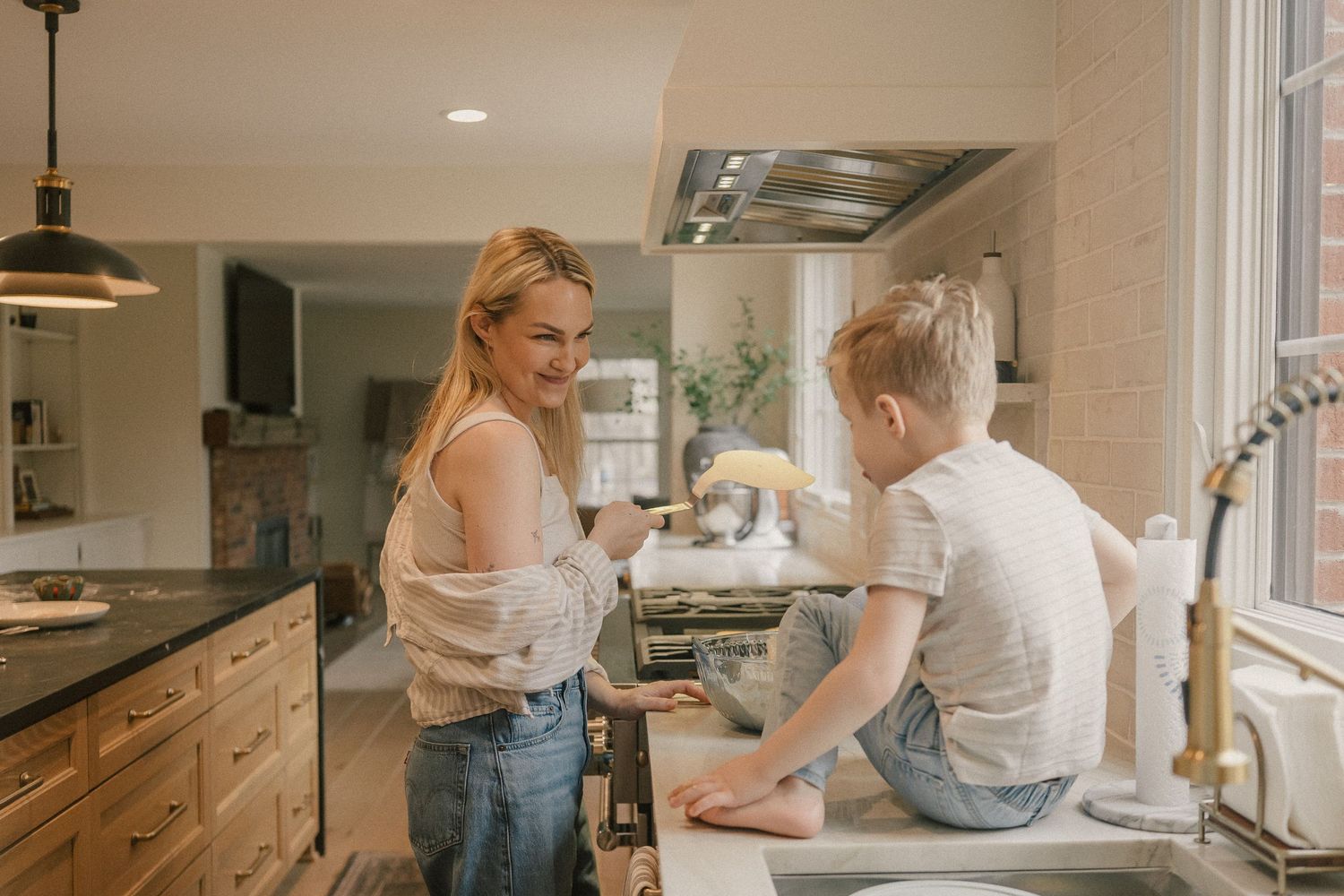 Smiling mother and young child bonding while cooking together at a bright white kitchen counter.