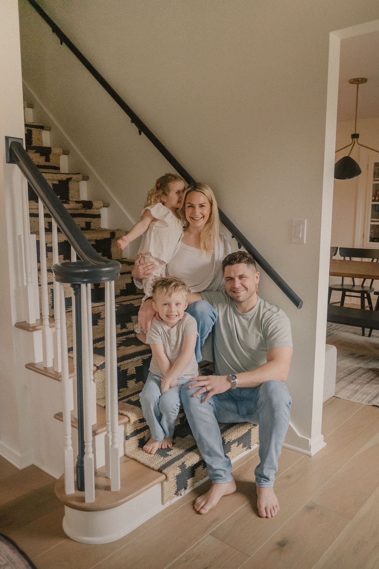 A smiling family of four poses together on a staircase in their modern home.