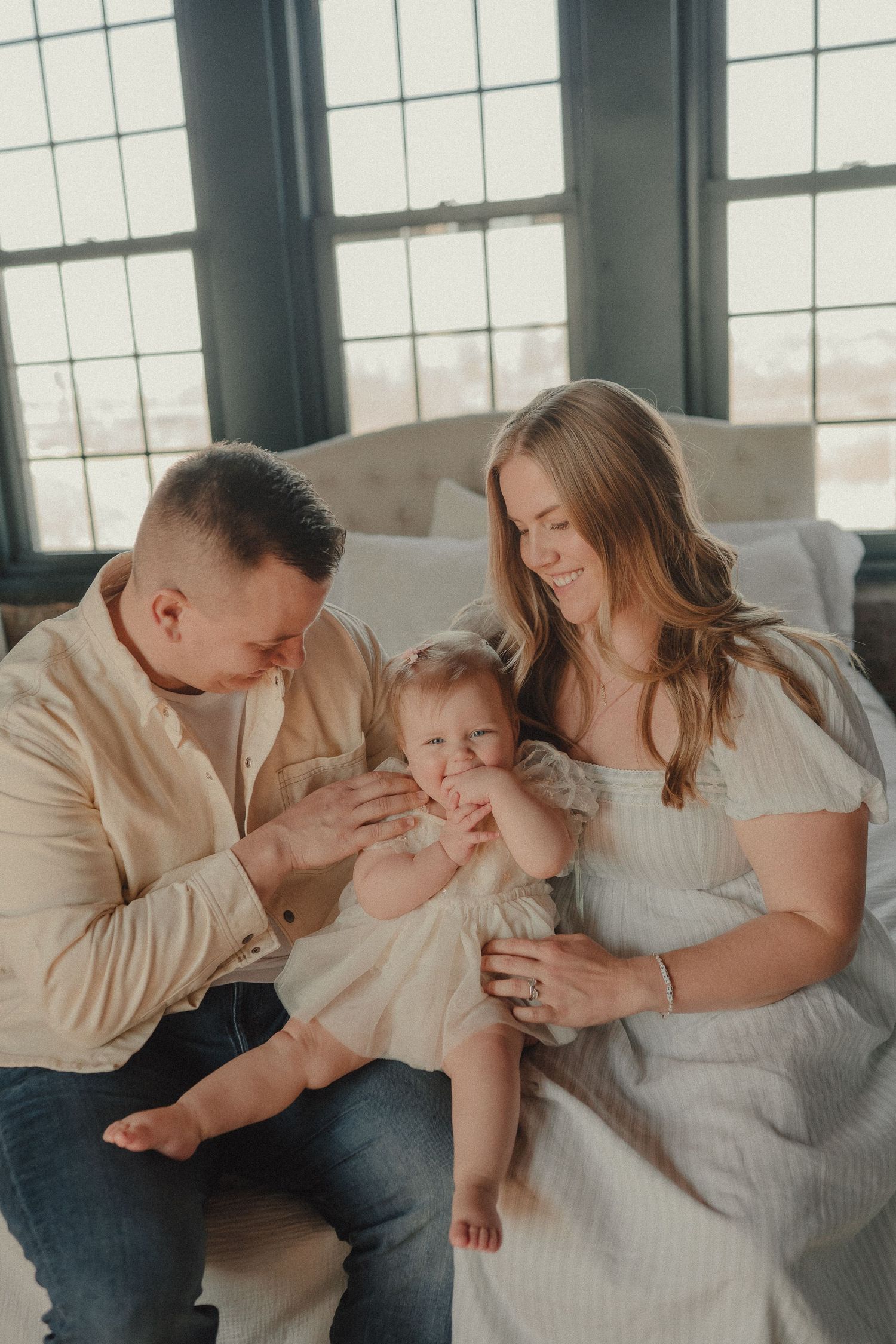 A loving family of three sits together near large windows in a bright, airy room.