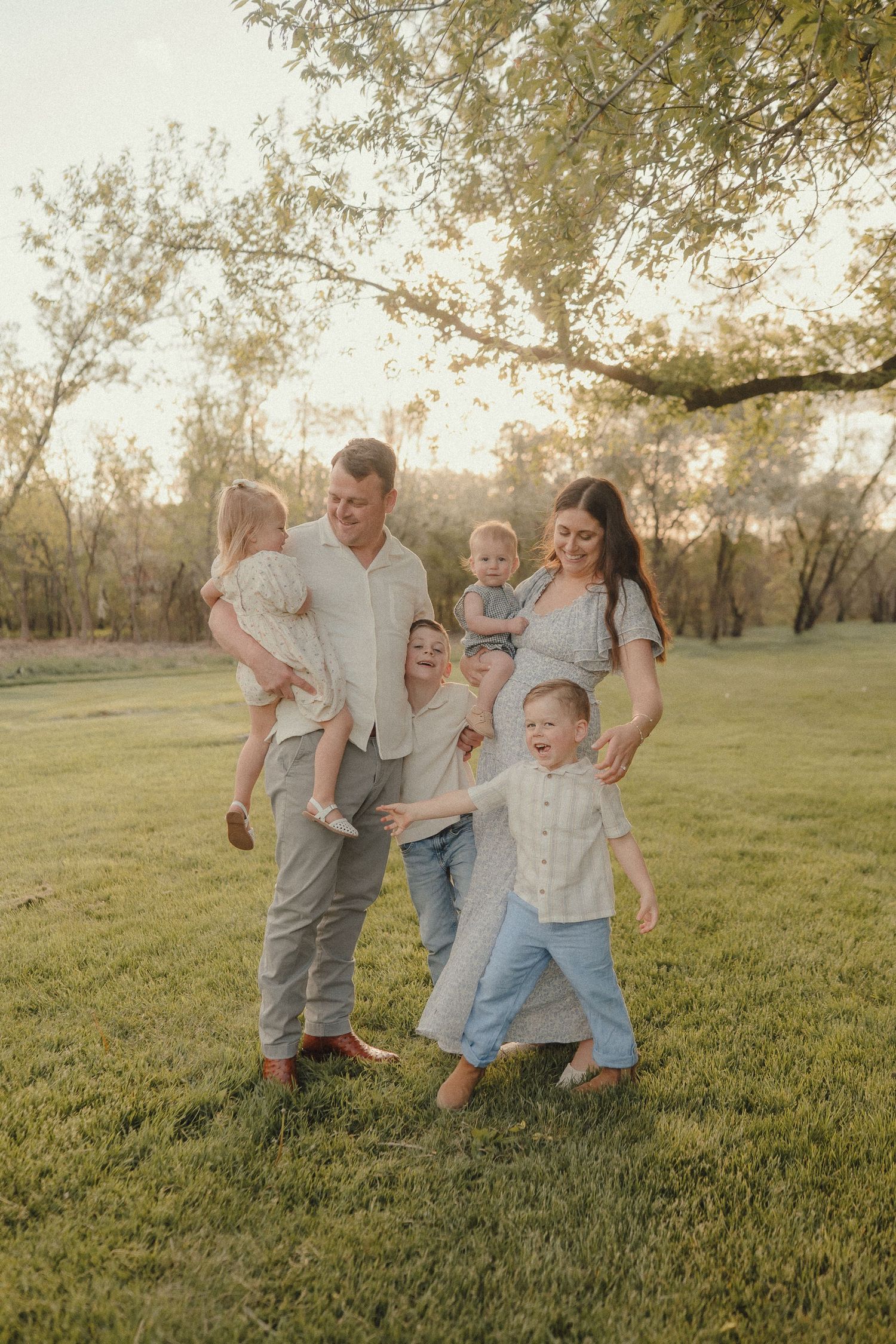 Happy family with four children laughing and playing together on green grass at sunset.