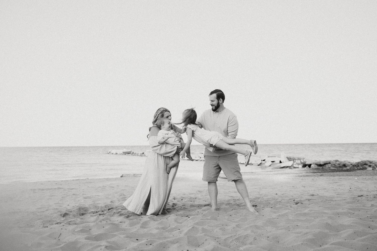 Black and white photo of a family of three playing on a sandy beach near the ocean.