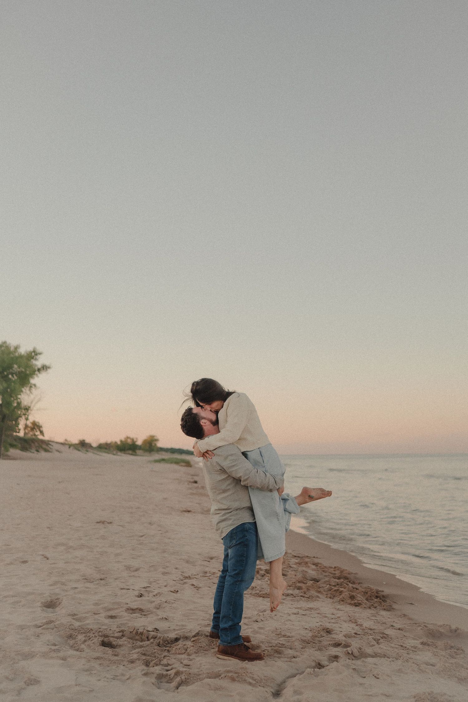 Romantic couple kissing on sandy beach at sunset with ocean in the background.