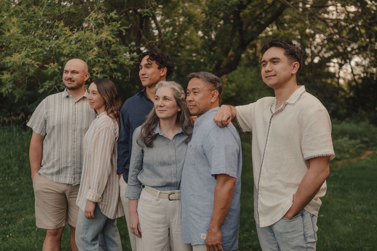 A diverse family of six poses together outdoors in a lush green park during golden hour.