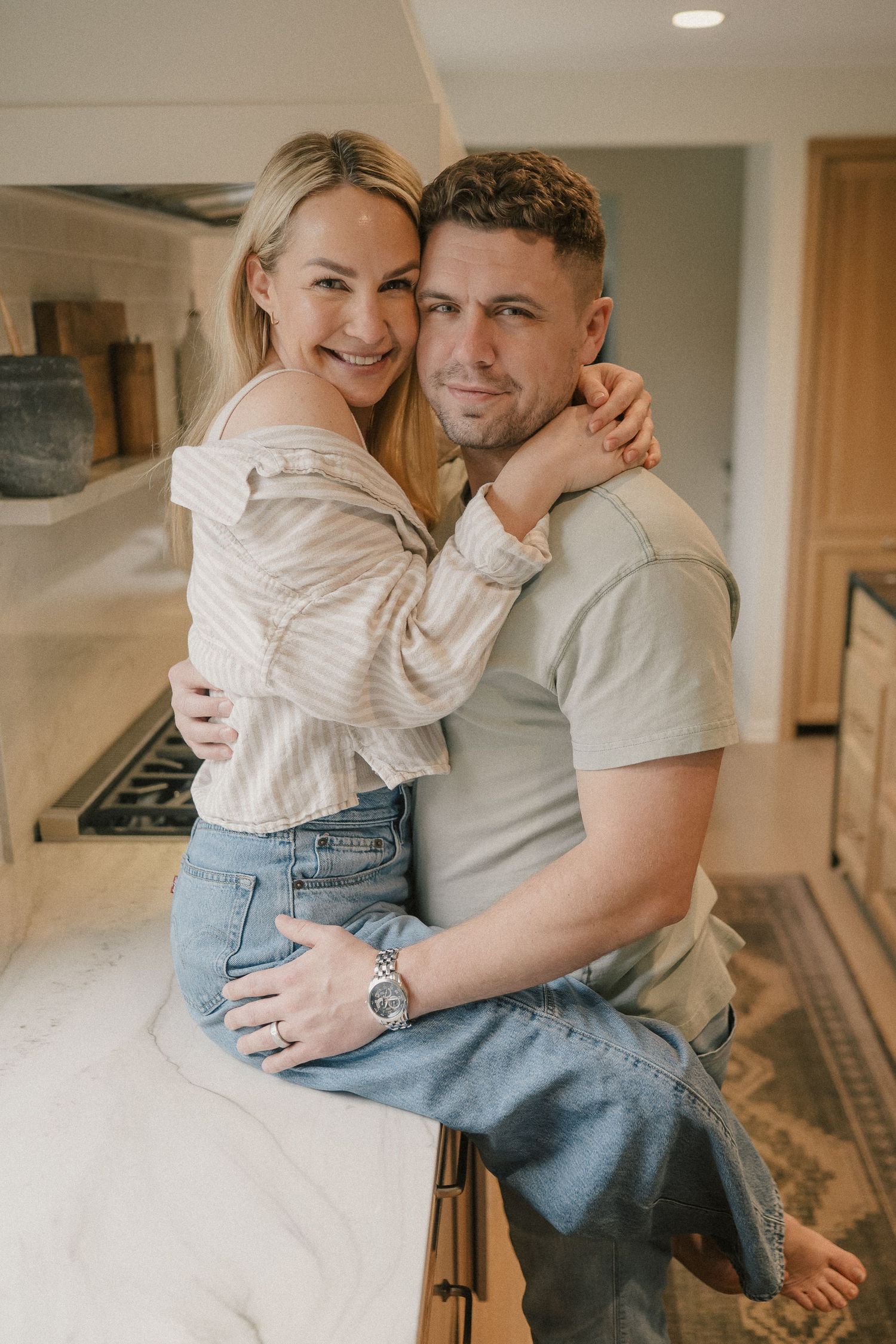 Smiling couple embracing while sitting on a kitchen counter in a warm modern home.
