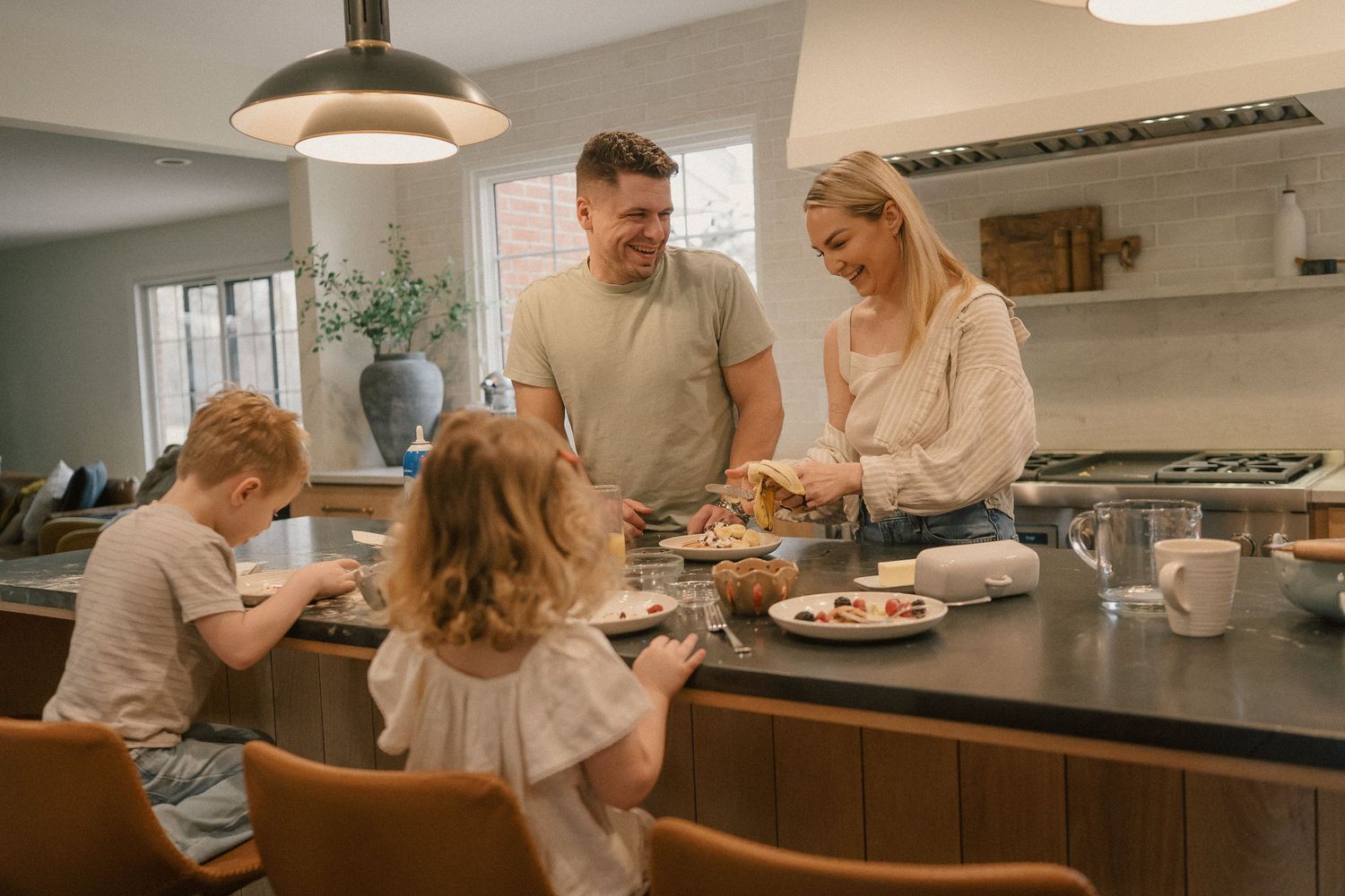 A happy family of four gathers around a kitchen island sharing a meal together.