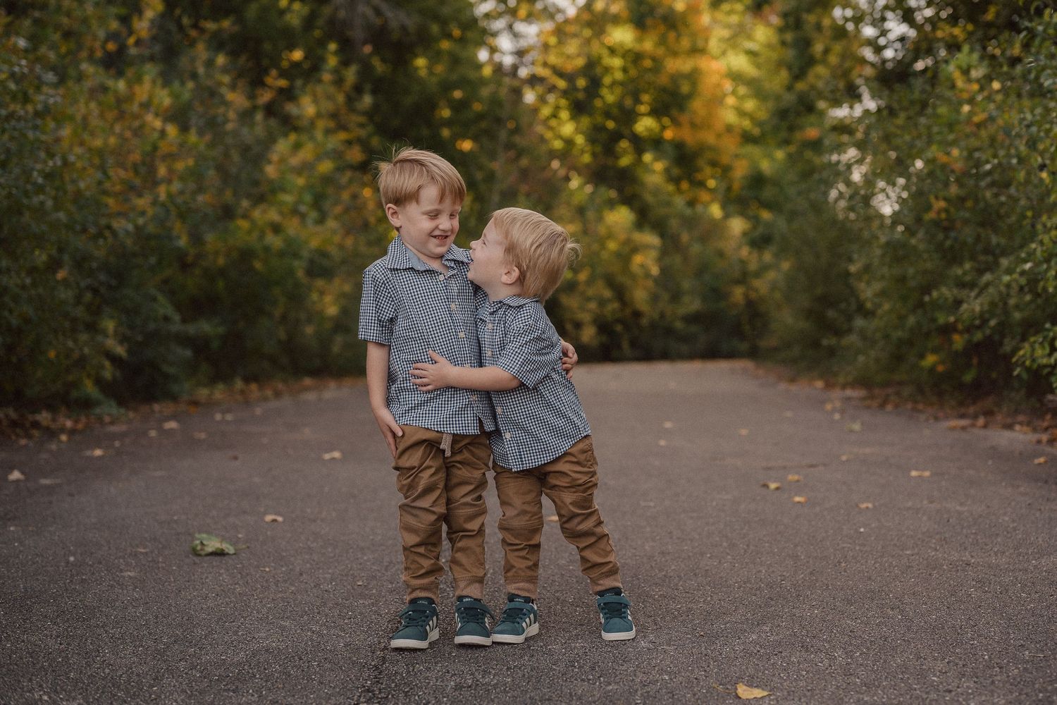 Two people in matching outfits walk hand in hand down a tree-lined autumn path.