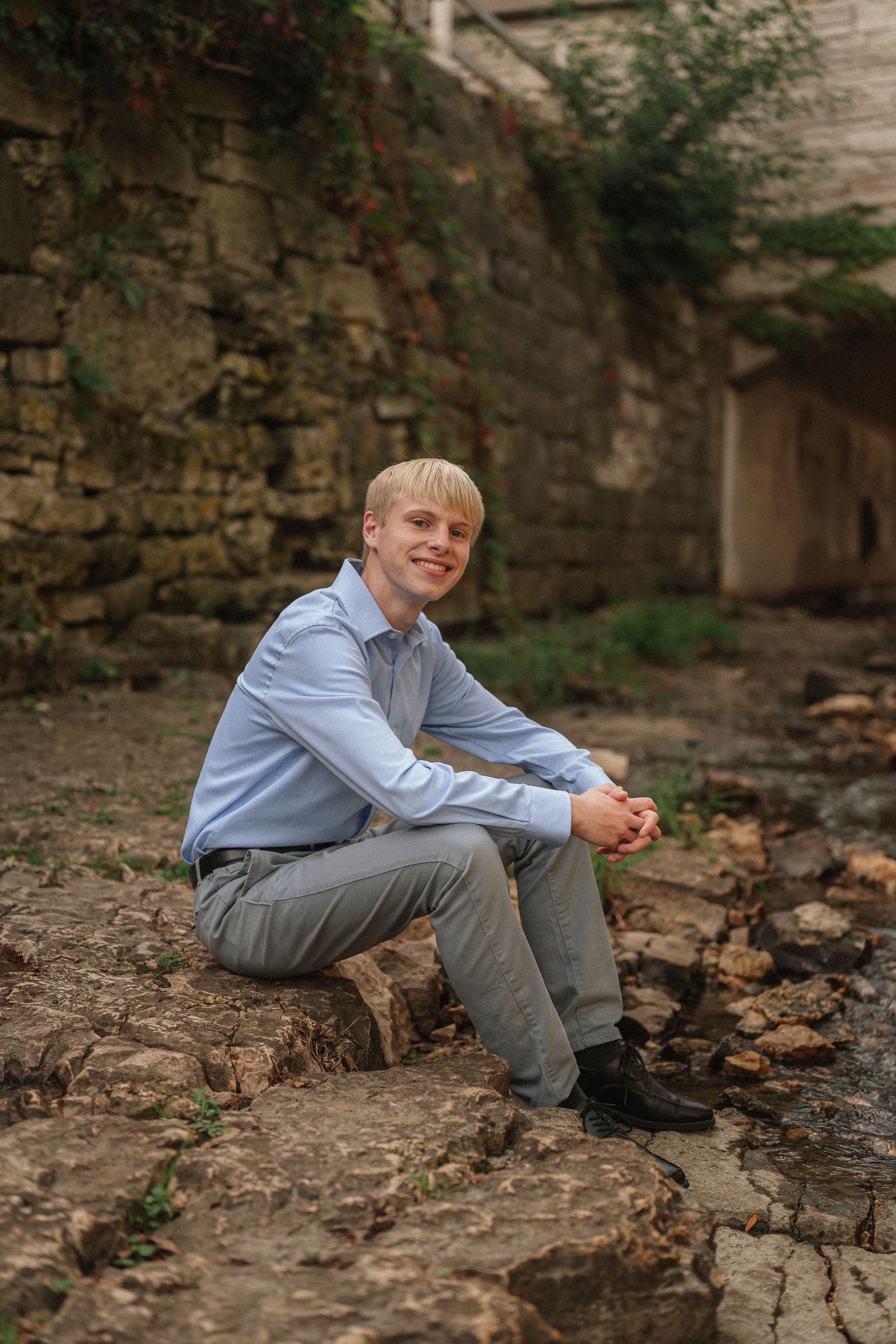 Student in light blue shirt and gray pants sits casually on stone steps in an outdoor setting.
